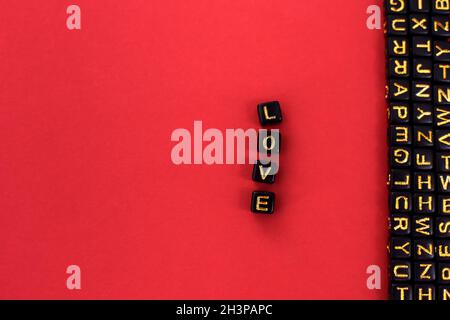 La parola amore scritto in lettere di legno. Lettere alfabetiche sui cubi. Su sfondo rosso Foto Stock