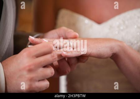 Primo piano della sposa di mettere un anello di nozze su govern dito. Giovane scambiare gli anelli di nozze. Foto Stock