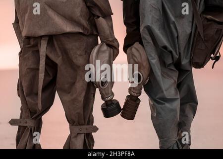 Due persone con maschere a gas e tute di protezione chimica sullo sfondo della terra morta bruciata. Foto Stock