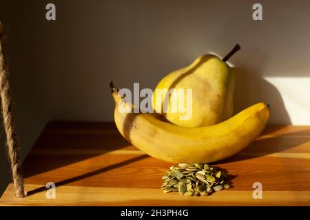 Pistacchi, banana e pera. Cibo sano. Frutta alla luce del sole. Vita morta di frutti gialli. Foto Stock