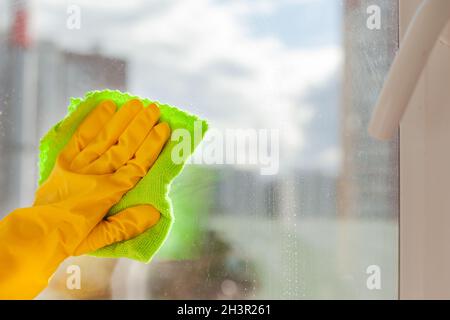 con la mano un guanto di gomma giallo si pulisce il vetro in primo piano Foto Stock