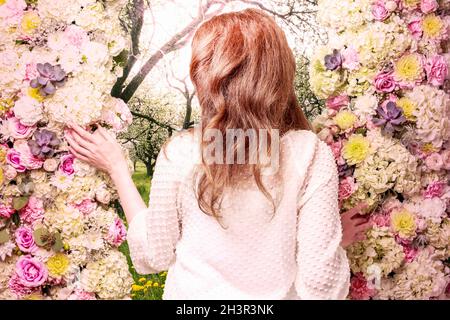 Donna che entra nel giardino segreto attraverso il cancello decorato con romantici ornamenti floreali con rose, dahlia, hortensia e fiori di garofano. Retro st Foto Stock