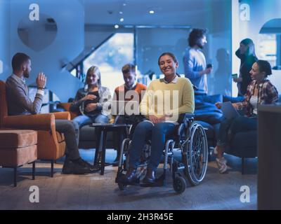 Ritratto di una donna d'affari disabile su una sedia a rotelle di fronte il suo team aziendale in ufficio Foto Stock