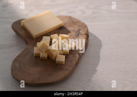 Piccolo blocco di formaggio stagionato affettato in piccoli pezzi su tavola di legno, poco profondo fuoco Foto Stock