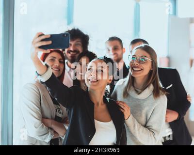 Gruppo di allegri colleghi che prendono selfie e gesturing mentre si levano in piedi nell'ufficio moderno. Foto Stock