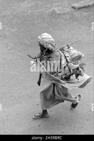 Africa, Sudan, nei pressi di Wad Madani 1976. Un povero uomo musulmano che cammina portando una borsa sulla schiena su un bastone. Foto Stock