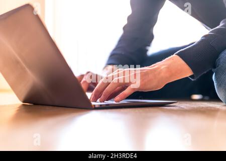 Il giovane uomo con un moderno computer portatile è seduto sul pavimento in legno Foto Stock