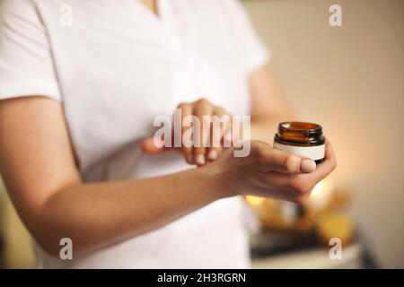 Crop cosmetologist applicare crema viso in salone Foto Stock
