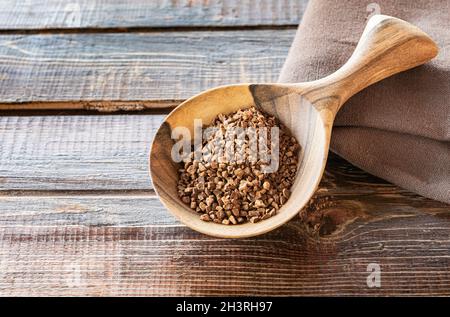 Primo piano della cicoria istantanea granulata. Granulas sono in grande cucchiaio di legno artigianale su tavola grezza fatta di tavole di legno naturale marrone con crepe. Foto Stock