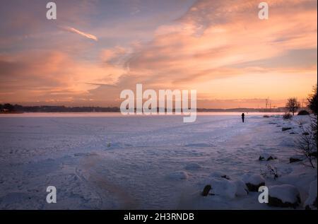 Tramonto invernale sul mare ghiacciato. Una silhouette di una donna che cammina sul ghiaccio. Foto Stock