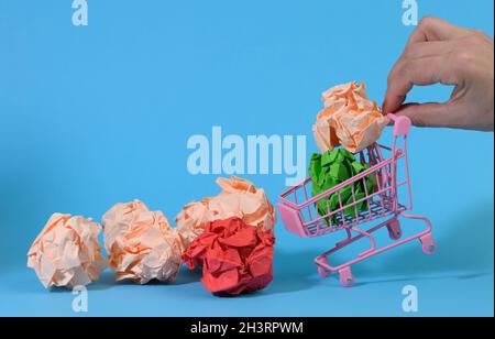 La mano tiene un carrello di metallo in miniatura con sfere di carta di menta su uno sfondo blu Foto Stock