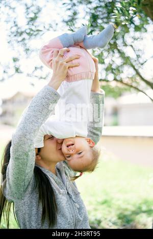 La mamma sorridente solleva la bambina capovolta e la bacia sulla guancia Foto Stock