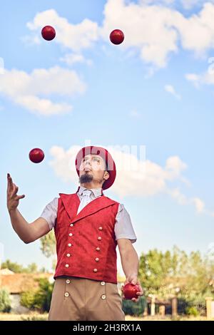 Da sotto giocoliere maschio in costume giocoleria palline rosse durante lo spettacolo nella soleggiata giornata estiva nel parco Foto Stock