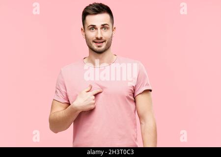 Stupito il giovane uomo che guarda sorpreso puntando se stesso, assicurandosi che sentì righ su sfondo rosa Foto Stock
