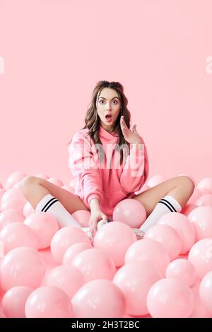 Giovane donna alla moda sorpresa con palloncini rosa su sfondo pastello rosa Foto Stock