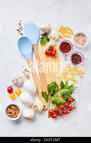 Fondo alimentare con diversi tipi di pasta, pomodori, erbe, funghi, uova, condimenti sparsi su sfondo di marmo chiaro Foto Stock