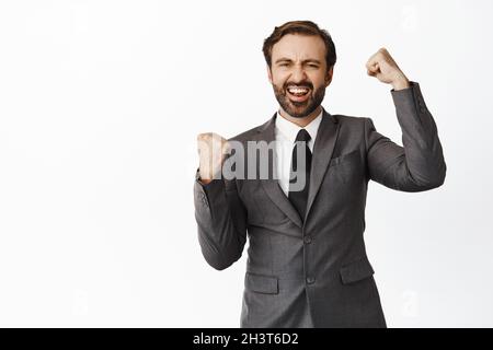Entusiasta uomo d'affari fortunato che vince e festeggia, gridando con gioia e pugno pompe, trionfando, raggiungere obiettivo, successo, sfondo bianco Foto Stock