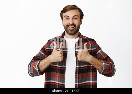 L'uomo adulto entusiasta mostra i pollici in su e sorride, sostiene l'idea grande, levandosi in piedi su sfondo bianco Foto Stock