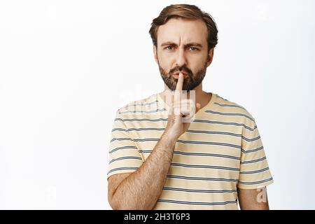 Ritratto di uomo arrabbiato che fremette e guarda dispiaciuto, dire di essere tranquillo, spoldante persona forte, gesto di chiusura, in piedi su sfondo bianco Foto Stock