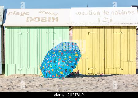 Persona che riposa sotto un ombrellone blu vicino a colorate capanne da spiaggia. Berck-Plage, Costa d'Opale, Francia Foto Stock