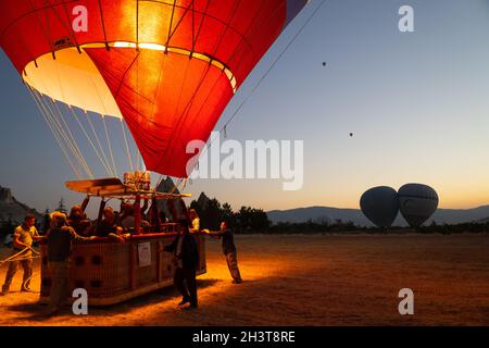 GOREME, TURCHIA - 3 AGOSTO 2021: Persone posizione per decollo di un pallone ad aria calda pieno di turisti, mentre il capitano accende il bruciatore fiamma an Foto Stock