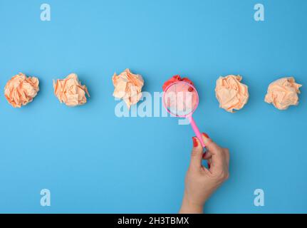 La mano femmina tiene una lente di ingrandimento sopra le sfere di carta arricciate. Concetto di ricerca e selezione di idee, brainstorming Foto Stock