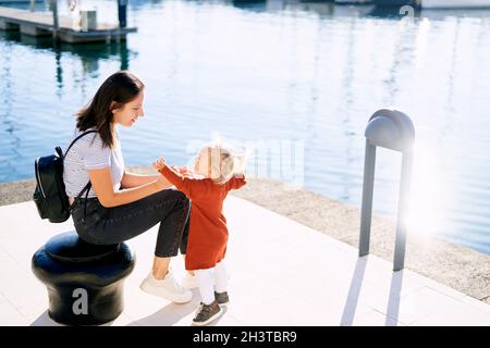 La donna sta guardando la sua bambina mentre si siede sopra un molo per barche Foto Stock