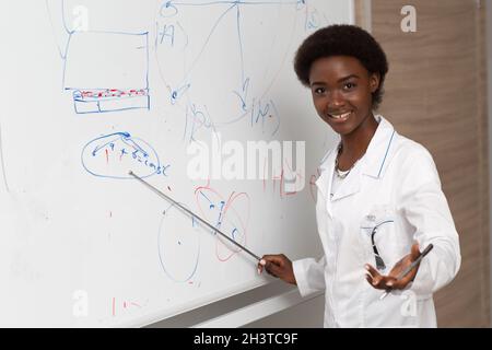 L'insegnante di matematica della donna afroamericana sta alla lavagna con puntatore Foto Stock