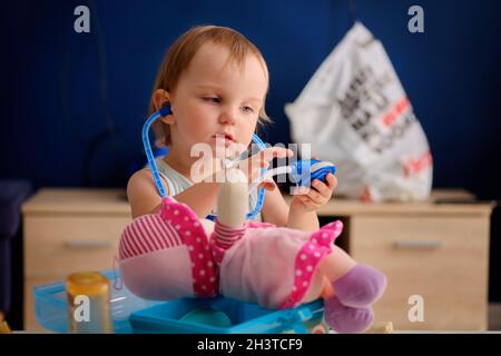 carina ragazza bionda sta giocando medico con la sua bambola rosa straccio Foto Stock