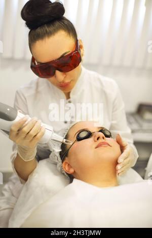 Donna che tratta il volto del cliente con il laser Foto Stock