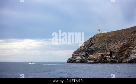 Faro situato sul capo Tamelos a Tzia isola, Cicladi destinazione estiva Grecia. Edificio del faro sulla scogliera rocciosa di Kea in un'onda egea Foto Stock