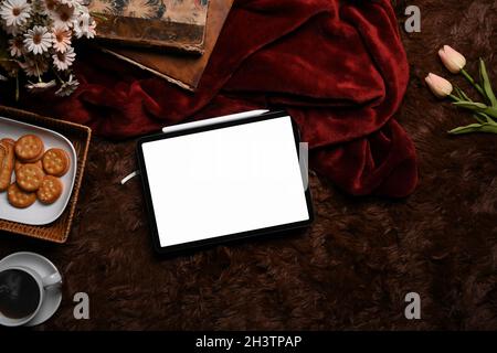 In alto visualizzate tablet digitale, tazza di caffè, biscotti e libri su un soffice tappeto. Foto Stock