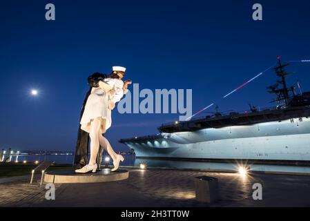 La Statua della resa incondizionata con la Luna in testa durante l'ora blu. San Diego, California, Stati Uniti. La USS Midway è sullo sfondo. Foto Stock