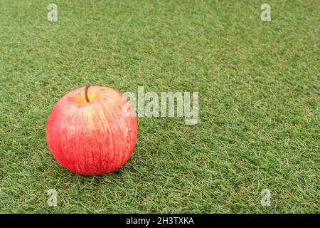 Faux mele rosse su erba sintetica. Per la coltivazione di mele nel Regno Unito, mele inglesi, industria britannica del sidro, ottobre Apple Day, prodotti britannici, uso di plastica Foto Stock