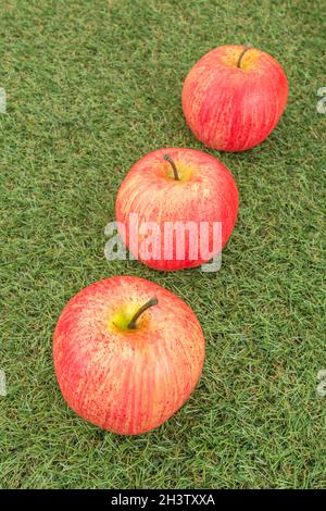 Faux mele rosse su erba sintetica. Per la coltivazione di mele nel Regno Unito, mele inglesi, industria britannica del sidro, ottobre Apple Day, prodotti britannici, uso di plastica Foto Stock