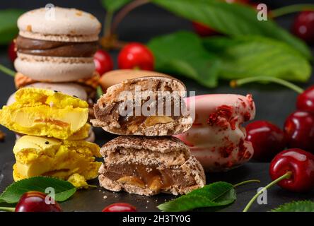 Pila di macaron multicolore e ciliegie rosse mature su sfondo di legno blu Foto Stock