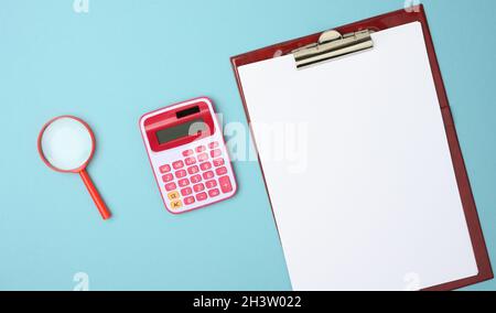 Calcolatrice rosa, cartella con fogli bianchi vuoti e lente di ingrandimento nera su sfondo blu Foto Stock