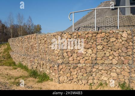 struttura ingegneristica in pietra dietro la rete metallica per rafforzare la riva del fiume vicino al ponte stradale Foto Stock