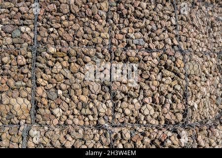 struttura ingegneristica in pietra dietro la rete metallica per rafforzare la riva del fiume vicino al ponte stradale Foto Stock