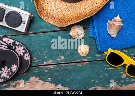 Concetto di vacanza: Tavolo in legno d'epoca con accessori per le vacanze: Cappello di paglia, occhiali da sole, infradito, conchiglie, macchina fotografica e bagno d'epoca Foto Stock