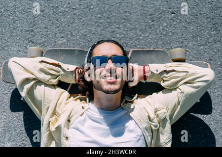 Ragazzo rilassato con occhiali da sole sdraiati su uno skateboard. Foto Stock