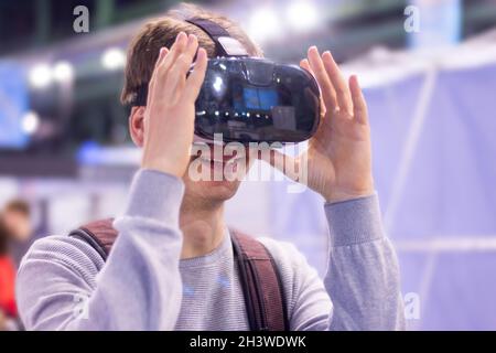 Il giovane uomo che indossa occhiali per realtà virtuale su una fiera è divertente Foto Stock