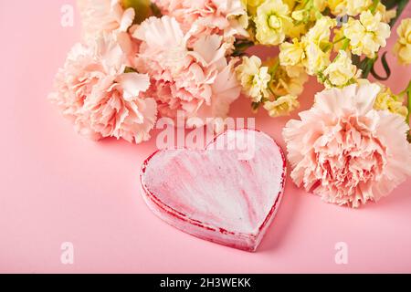 Bouquet di garofani rosa e mattiola gialla con cuore decorativo. Design concetto di saluto vacanza con bouquet garofano Foto Stock