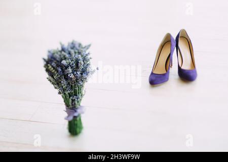 Un bouquet di lavanda e scarpe da donna con tacco alto viola su una texture di legno bianco. Foto Stock