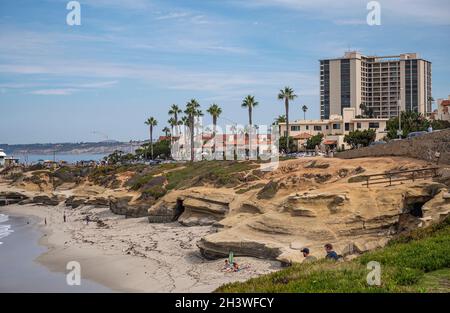 La Jolla, California, Stati Uniti d'America - 3 ottobre 2021: Formazione di roccia di pietra marrone e grotte sulla spiaggia di WipEout con alto condominio edificio sopra sotto il blu clo Foto Stock