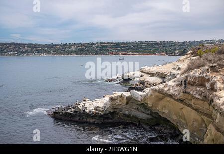 La Jolla, California, Stati Uniti d'America - 3 ottobre 2021: Primo piano di lato est rocce sporche della Cove con verde cintura di alloggiamento all'orizzonte che separa la nuvola blu Foto Stock