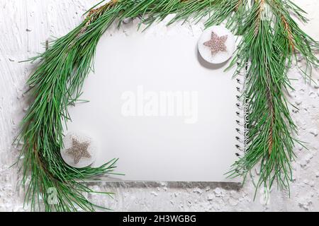 Blocco note con posto per testo con ramo di abete e stelle su sfondo bianco e gelido. Natale, Capodanno. Spazio di copia Foto Stock
