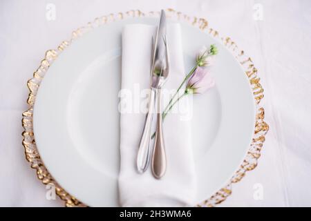 Ricevimento con cena al tavolo per matrimoni. Piatto bianco sulla parte superiore di un carattere jolly con bordi dorati. In un piatto bianco c'è un tovagliolo, un coltello, Foto Stock