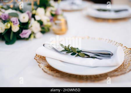 Ricevimento con cena al tavolo per matrimoni. Piatto bianco sulla parte superiore di un carattere jolly con bordi dorati. In un piatto bianco c'è un tovagliolo, un coltello, Foto Stock