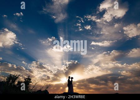 La sposa e lo sposo abbracciano teneramente la montagna ai raggi del sole che tramonta Foto Stock
